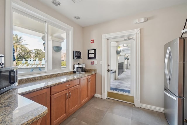 kitchen featuring light tile patterned floors, stone countertops, baseboards, appliances with stainless steel finishes, and brown cabinets