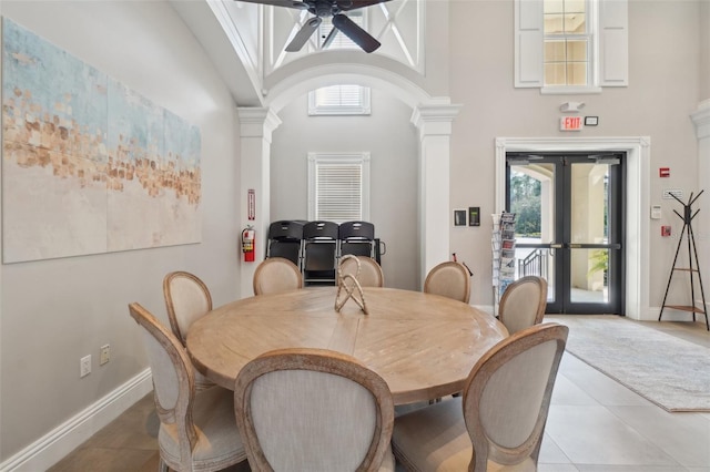 dining room featuring a towering ceiling, ornate columns, light tile patterned flooring, and french doors