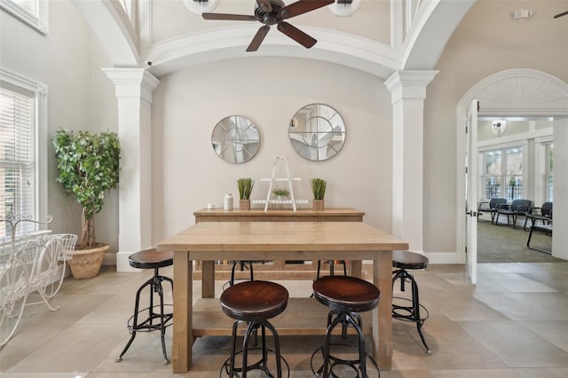 dining room featuring arched walkways, a high ceiling, a ceiling fan, baseboards, and decorative columns