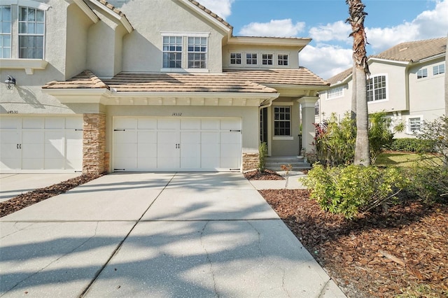 view of front of property with an attached garage, a tile roof, stone siding, driveway, and stucco siding