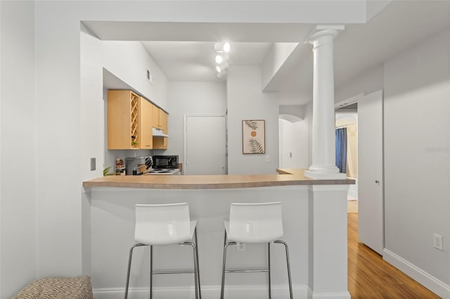 kitchen featuring light wood finished floors, visible vents, under cabinet range hood, ornate columns, and light brown cabinets