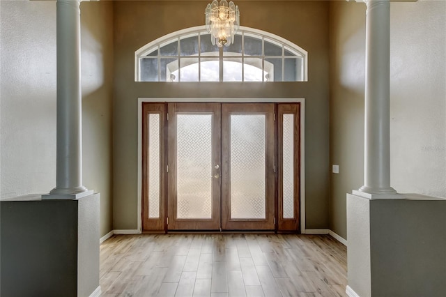 foyer entrance with light wood finished floors, decorative columns, baseboards, and a chandelier