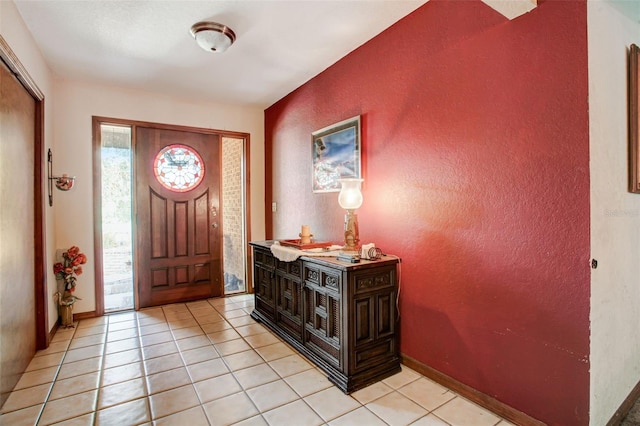 foyer entrance featuring light tile patterned floors, a textured wall, and baseboards