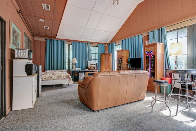 carpeted living room featuring vaulted ceiling, wood walls, visible vents, and a healthy amount of sunlight