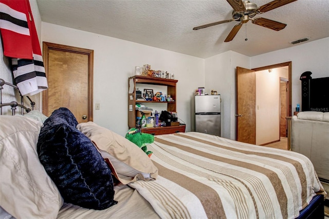 bedroom featuring visible vents, ceiling fan, a textured ceiling, and freestanding refrigerator