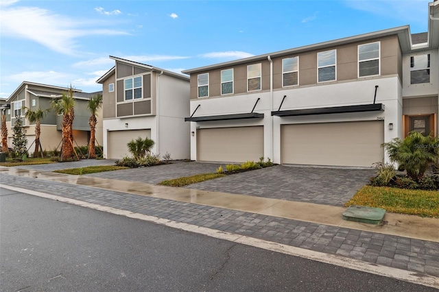 multi unit property featuring stucco siding, an attached garage, and decorative driveway