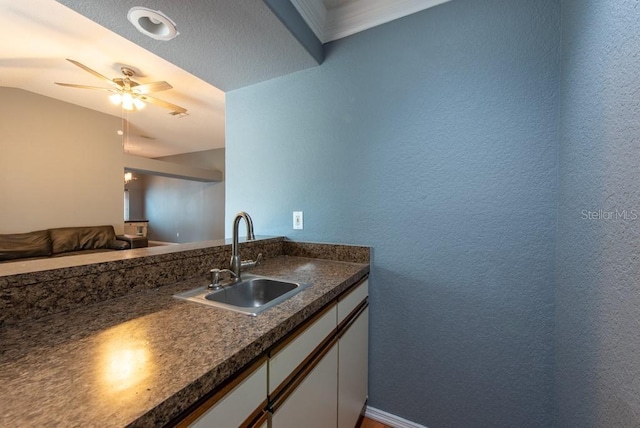 kitchen with dark countertops, a ceiling fan, white cabinets, a sink, and a textured wall