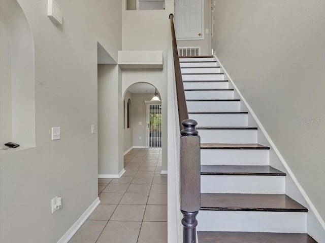 staircase featuring arched walkways, baseboards, visible vents, tile patterned flooring, and a high ceiling