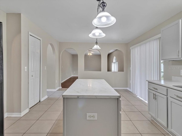 kitchen featuring light tile patterned floors, arched walkways, light stone counters, a kitchen island, and hanging light fixtures