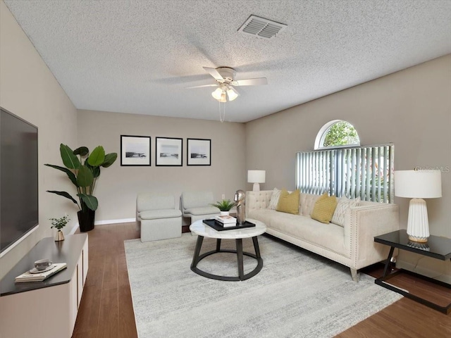 living room with a ceiling fan, visible vents, dark wood finished floors, and a textured ceiling