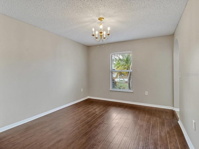 spare room featuring dark wood-style floors, baseboards, arched walkways, and a notable chandelier