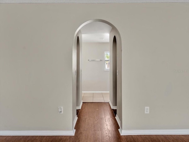 corridor featuring baseboards, arched walkways, and wood finished floors