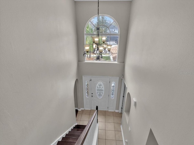 foyer with a chandelier, light tile patterned floors, arched walkways, a high ceiling, and baseboards