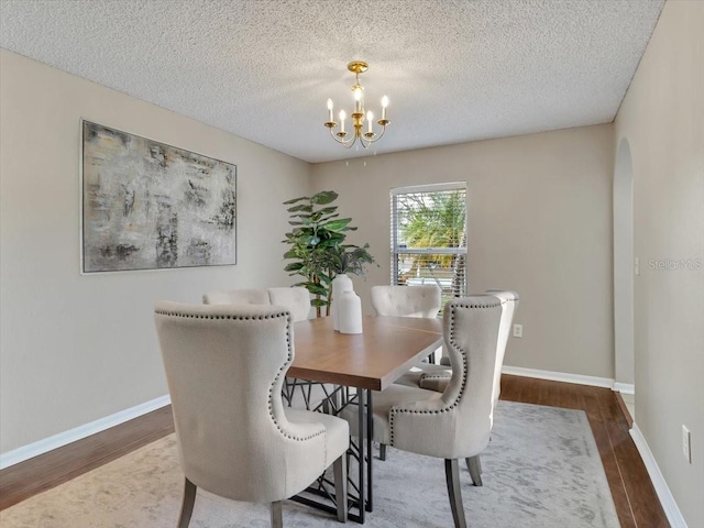 dining area with a chandelier, arched walkways, wood finished floors, a textured ceiling, and baseboards