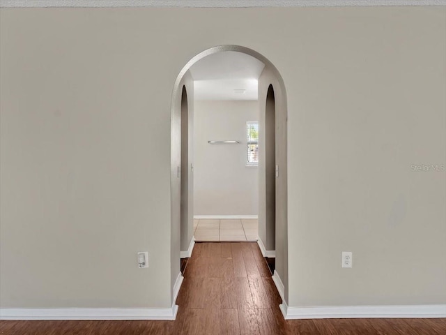 hall with arched walkways, wood finished floors, and baseboards