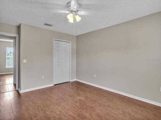 unfurnished bedroom with wood finished floors, a textured ceiling, baseboards, a closet, and a ceiling fan
