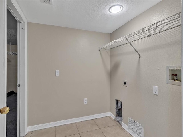 clothes washing area featuring electric dryer hookup, washer hookup, light tile patterned floors, baseboards, and a textured ceiling