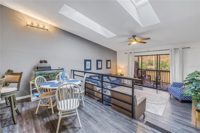 dining space featuring dark wood-style floors, vaulted ceiling with skylight, baseboards, and ceiling fan