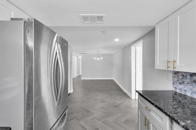 kitchen with visible vents, white cabinets, dark stone countertops, and freestanding refrigerator