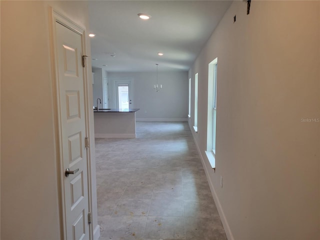 hall featuring a sink, baseboards, an inviting chandelier, and recessed lighting