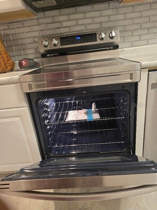 interior details with light countertops, white cabinets, decorative backsplash, and electric stove