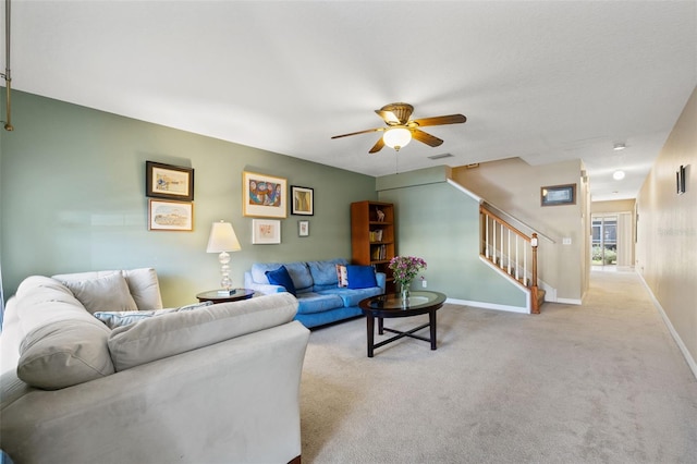 living area featuring baseboards, visible vents, light colored carpet, ceiling fan, and stairs