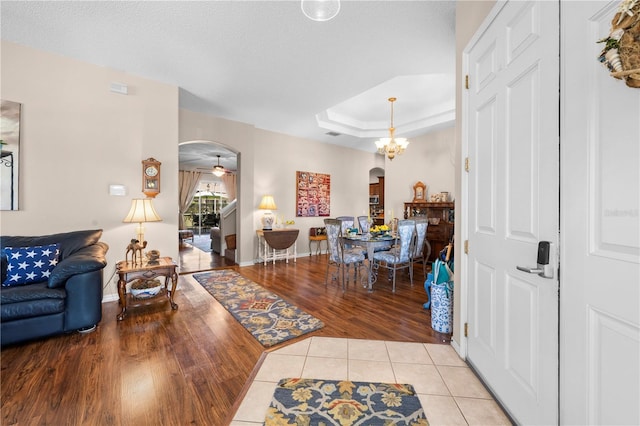 interior space featuring arched walkways, a notable chandelier, a tray ceiling, and light tile patterned floors