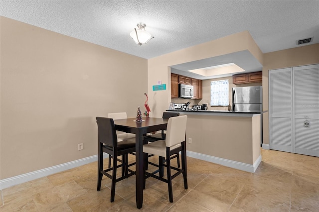 dining area with a textured ceiling, a tray ceiling, visible vents, and baseboards