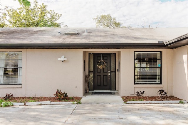 view of exterior entry with a shingled roof and stucco siding