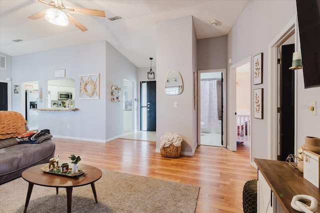 living room featuring light wood finished floors, baseboards, visible vents, and vaulted ceiling