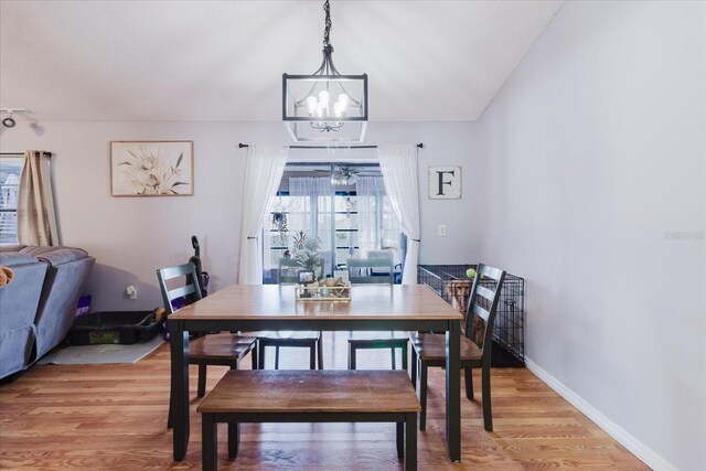 dining room with vaulted ceiling, light wood-style flooring, baseboards, and ceiling fan with notable chandelier