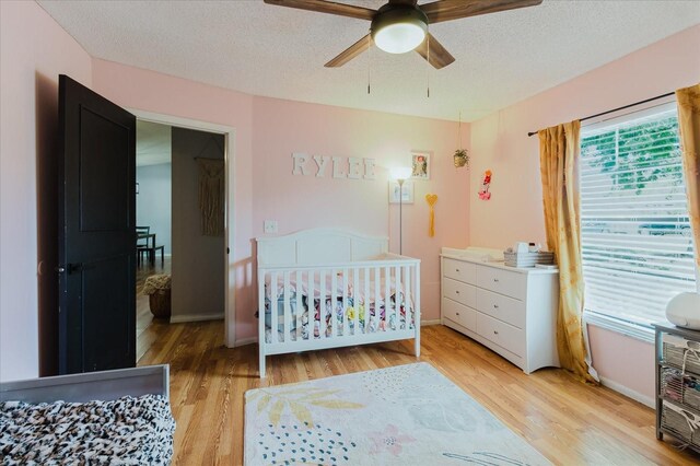 bedroom with a textured ceiling, a ceiling fan, baseboards, light wood-style floors, and a nursery area