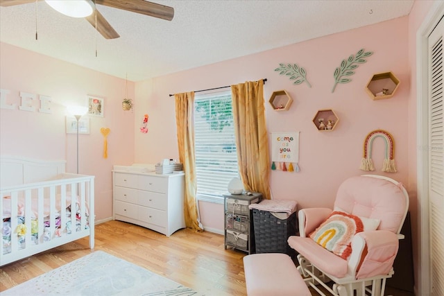 bedroom featuring a nursery area, a closet, ceiling fan, a textured ceiling, and light wood-type flooring