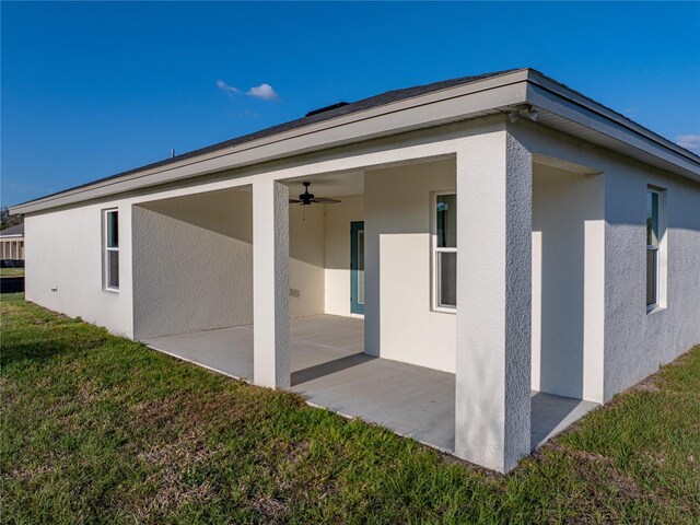 back of house featuring a ceiling fan, a patio area, a lawn, and stucco siding