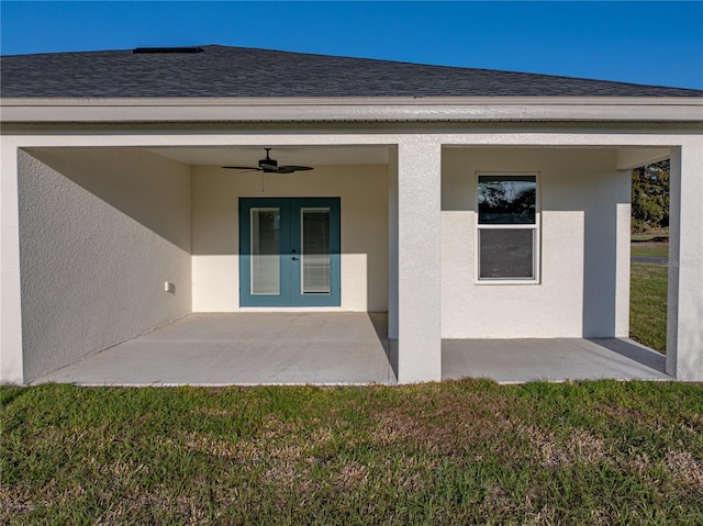 entrance to property with stucco siding, ceiling fan, a shingled roof, and french doors