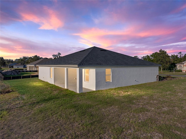 rear view of house with a shingled roof, a patio area, a lawn, and stucco siding