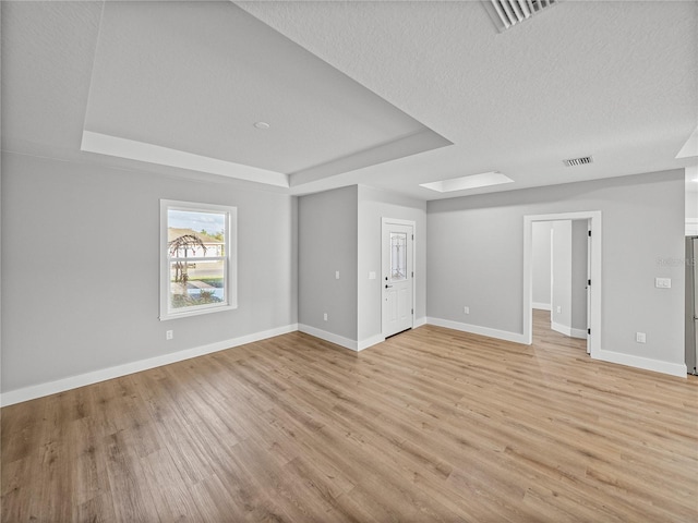 spare room featuring light wood-style flooring, visible vents, and a raised ceiling