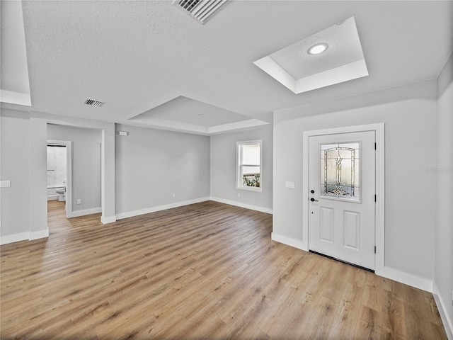 foyer entrance with light wood finished floors, a raised ceiling, visible vents, and baseboards