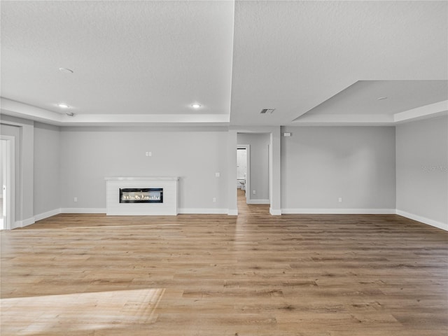 unfurnished living room featuring light wood-type flooring, visible vents, a tray ceiling, and a glass covered fireplace