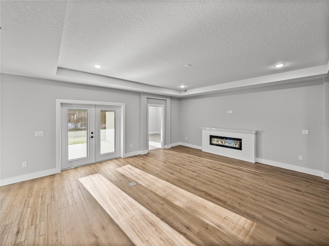 unfurnished living room featuring french doors, a glass covered fireplace, a textured ceiling, wood finished floors, and baseboards