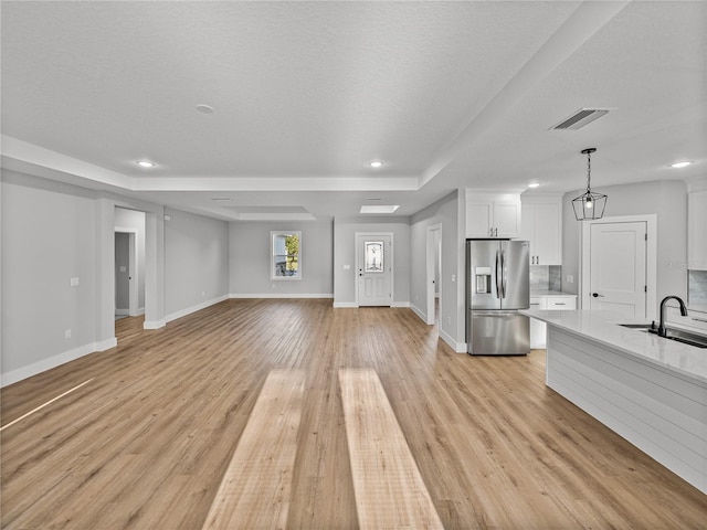 unfurnished living room with visible vents, a sink, a textured ceiling, light wood-type flooring, and baseboards