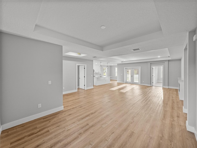 unfurnished living room with light wood-type flooring, a raised ceiling, baseboards, and french doors