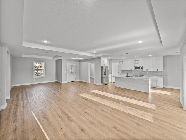 unfurnished living room featuring a sink, a raised ceiling, light wood-style flooring, and baseboards