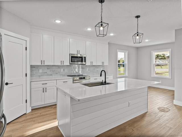 kitchen featuring an island with sink, decorative light fixtures, stainless steel appliances, white cabinetry, and a sink