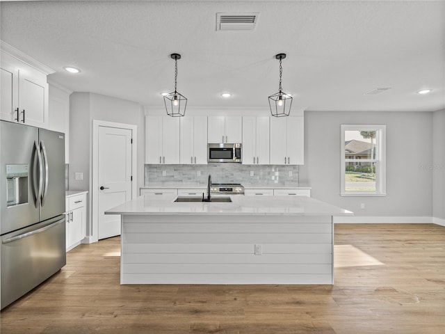 kitchen with an island with sink, appliances with stainless steel finishes, light countertops, and decorative light fixtures