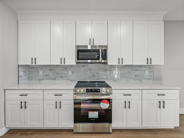 kitchen with light stone countertops, appliances with stainless steel finishes, white cabinets, and wood finished floors