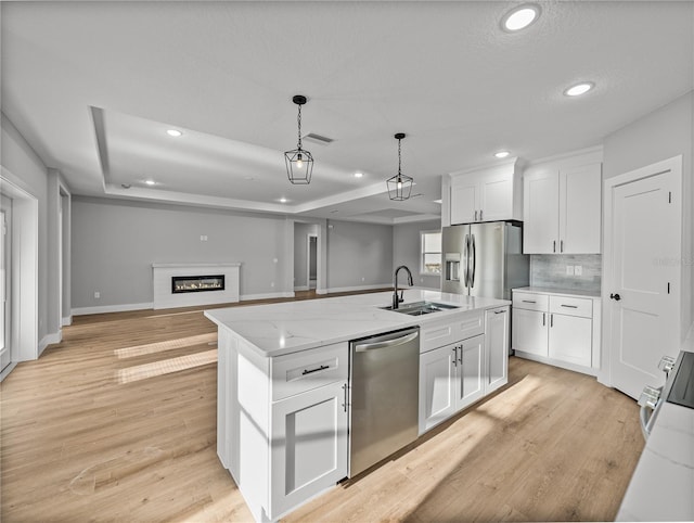 kitchen featuring a sink, white cabinetry, open floor plan, appliances with stainless steel finishes, and a center island with sink