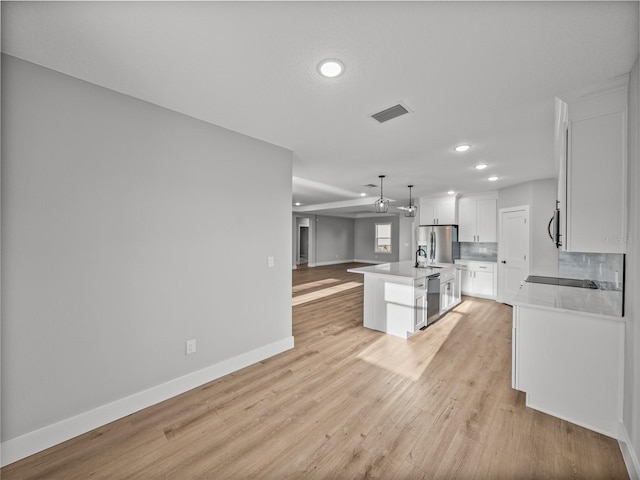 kitchen featuring white cabinets, open floor plan, hanging light fixtures, a kitchen island with sink, and light countertops