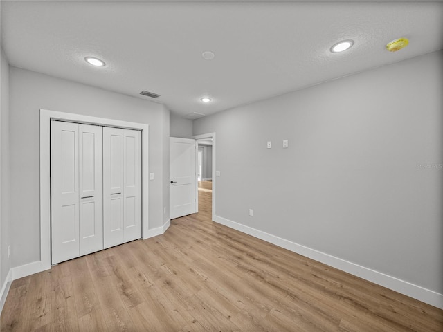 unfurnished bedroom with a closet, visible vents, light wood-style flooring, a textured ceiling, and baseboards