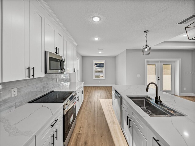 kitchen with stainless steel appliances, a sink, white cabinetry, hanging light fixtures, and french doors